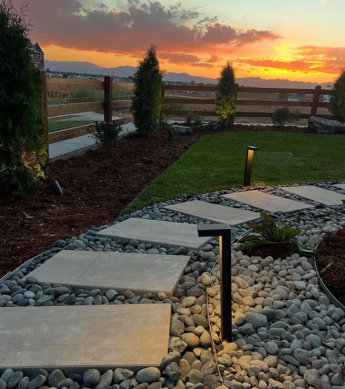 Landscaped bed with river rock, stepping stones and path lighting at sunset