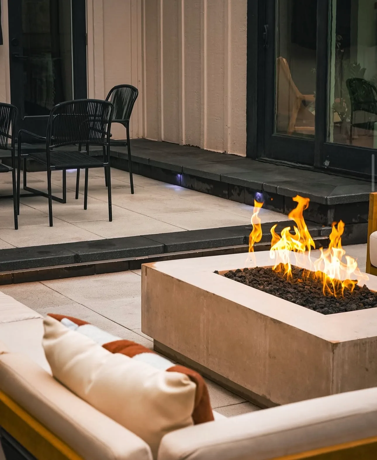 Rectangular gas fire pit lit beside outdoor seating on a finished patio