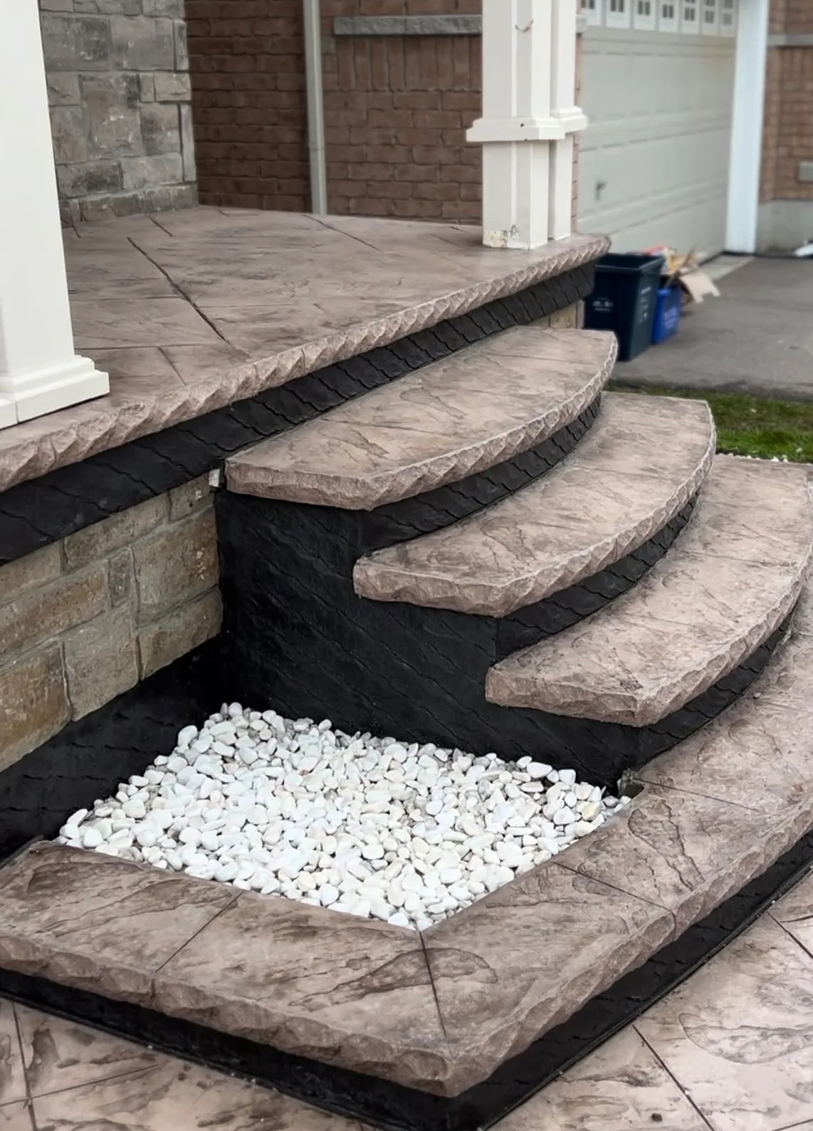 Dark stamped concrete steps stepping down over a bed of white rock