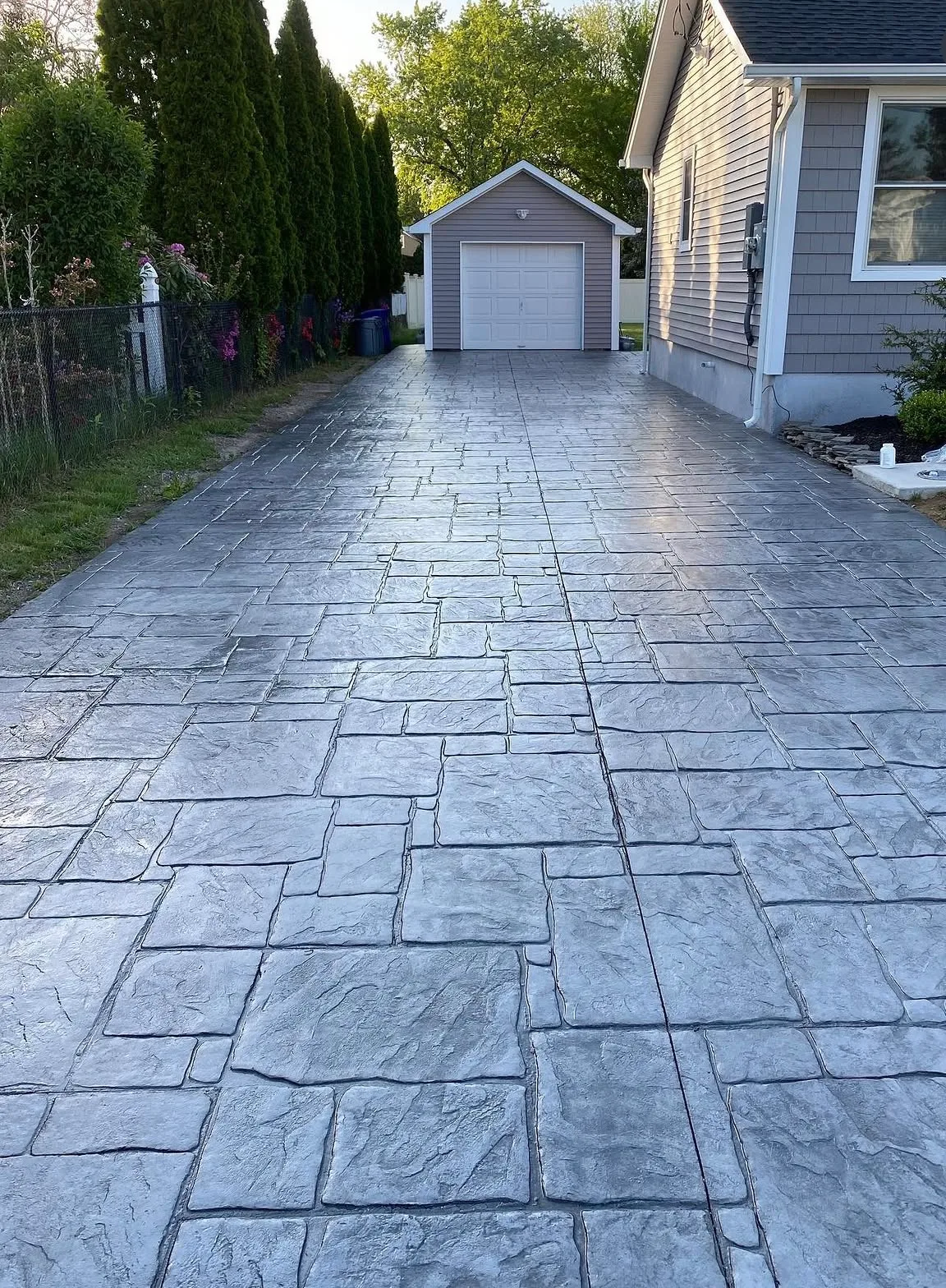 Grey stamped concrete driveway running between a house and a fence line