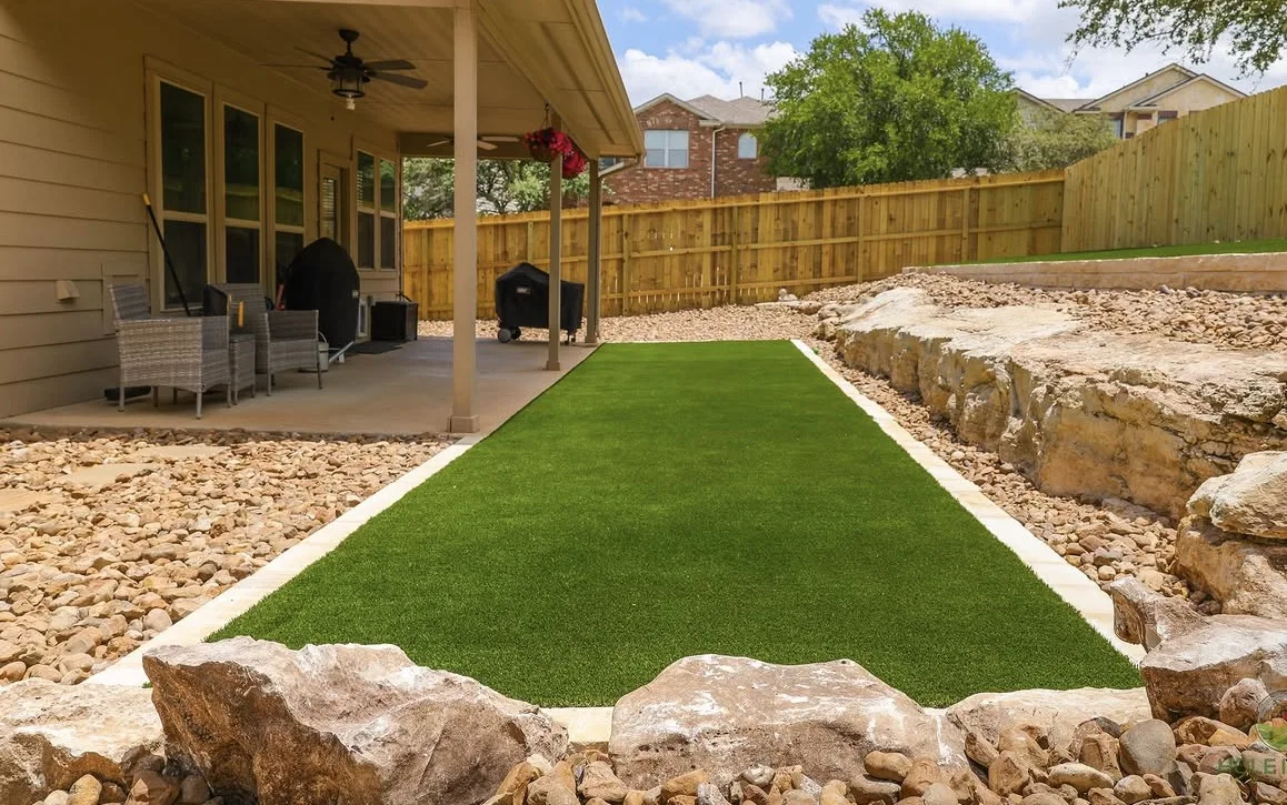 Artificial turf run bordered with rock and boulders beside a covered patio