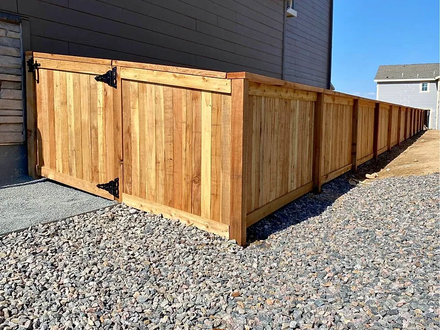 New cedar privacy fence with a matching gate along a gravel side yard
