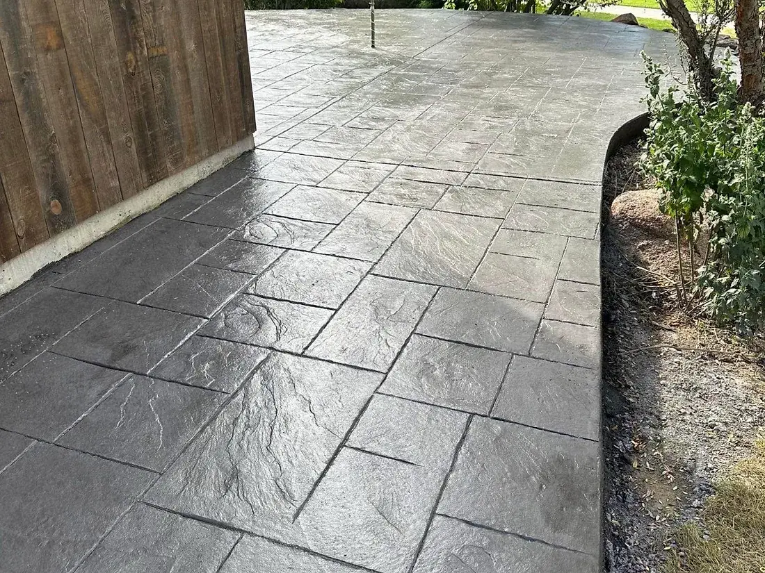 Stamped concrete walkway curving past a lawn and a rock border