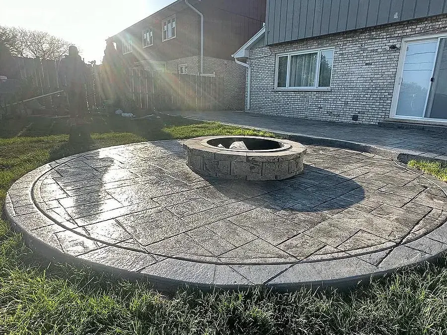 Circular stamped concrete patio built around a stone fire pit in morning sun